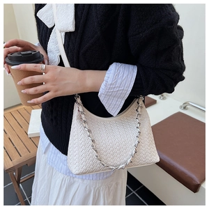 Detail of white woven crescent shoulder bag with silver chain strap in a cafe setting