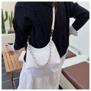 Detail of white woven shoulder bag with silver chain worn by a model in a minimalist setting