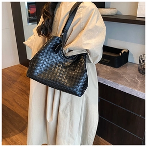 Detail of a large black woven leather tote bag worn by a model in a lifestyle setting