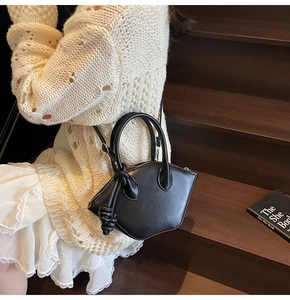 Black geometric mini shell bag with woven rope detail shown in a lifestyle street setting