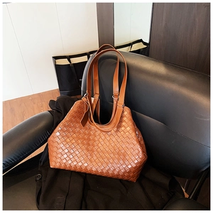 Close-up of brown woven leather tote bag with dual handles on a leather chair