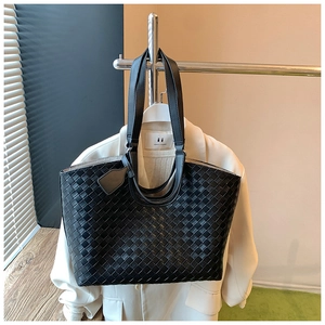 Detail of black woven tote bag hanging on a hanger alongside a stylish white blazer