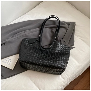 Detail of black woven tote bag texture and thin strap on a minimalist blazer backdrop