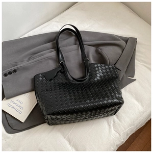 Close-up of the woven black leather texture and long handles on a large tote bag