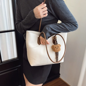 White lychee pattern leather tote bag with brown handles and a plush bear charm accessory