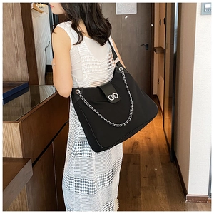 Side view of black hobo bag with silver chain strap and metal lock shown on a model