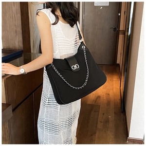 Detail of black tote bag with silver chain decor and metal buckle on a shoulder strap