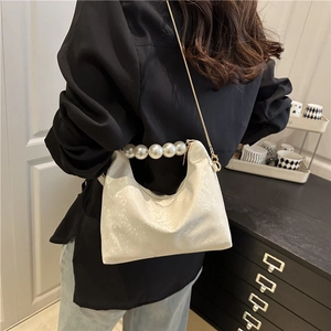 White snakeskin dumpling bag with pearl handle and gold chain strap shown on model