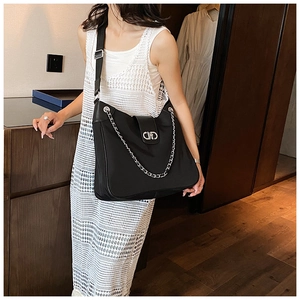 Detail of black tote bag with silver chain decor and metal buckle in a home setting