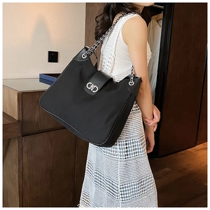 Close-up of black leather tote bag featuring a silver chain strap and metal CD clasp