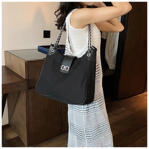 Close-up of a black leather tote featuring silver chain strap and metal logo clasp detail