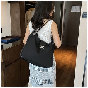 Detail of black shoulder bag with silver chain strap and CD metal clasp on white dress
