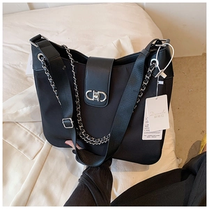 Detail of black nylon shoulder bag featuring a metal CD logo buckle and dual chain straps