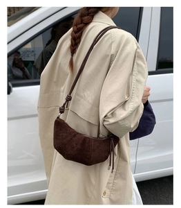 Détail du sac croissant en daim marron foncé avec plis piqués verticaux et gland de zip