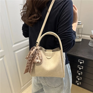 Borsa a secchiello beige minimalista con manico e foulard in seta indossata da modella