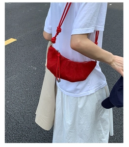 Détail du sac croissant en daim rouge avec bandoulière à nœud épais sur une robe blanche