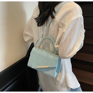 Close-up of light blue crossbody bag with woven texture flap and gold hardware detail