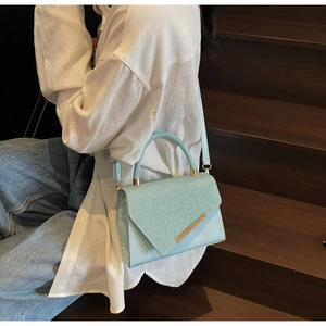 Close-up of light blue glitter handbag with V-cut flap and gold bar on wooden stairs