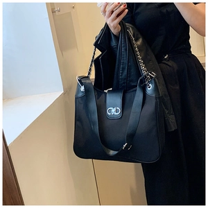 Detail of black soft leather tote with wide nylon strap, silver chain and metal buckle