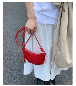 Gros plan du sac croissant en daim rouge avec nœud sur la bandoulière et robe blanche