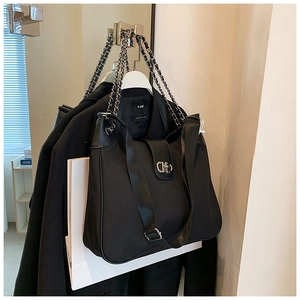 Detail of black tote bag with silver chain strap and metal buckle on suit background