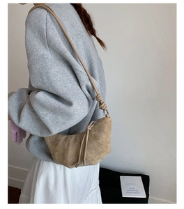 Gros plan d'un sac demi-lune en daim beige montrant le détail du gland et la texture mate