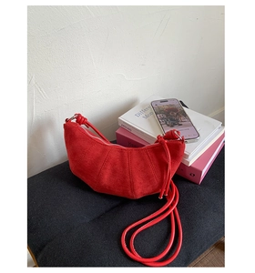Détail d'un sac demi-lune en daim rouge avec coutures segmentées sur un banc noir