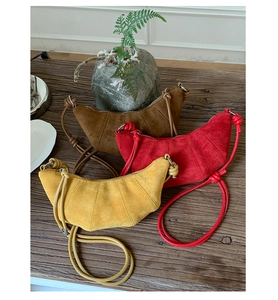 Gros plan de sacs bandoulière en daim marron, rouge et jaune sur une table en bois