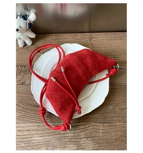 Gros plan d'un sac croissant en daim rouge avec bandoulière nouée et détails argentés