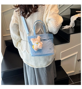 Détail d'un sac seau en toile bleue avec broderie RAH TOP et pendentif ours en peluche doux