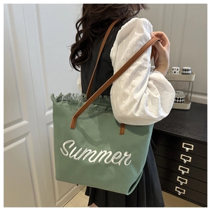 Dettaglio borsa tote in tela verde con ricamo Summer bianco e bordi con frange