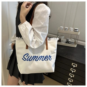 Detail of white canvas tote bag with blue Summer embroidery and brown leather straps