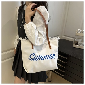 Close-up of blue Summer embroidery and fringe tassel detail on white canvas tote bag