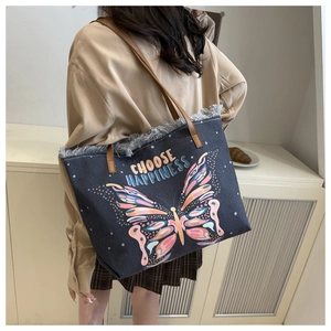 Detail of blue denim tote bag featuring fringe edges and colorful butterfly print