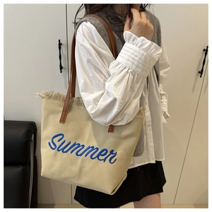 Dettaglio della borsa tote in tela beige con ricamo blu e finiture a frange