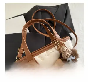 Close-up of cream bucket bag with embossed patterns and a brown fuzzy monster charm