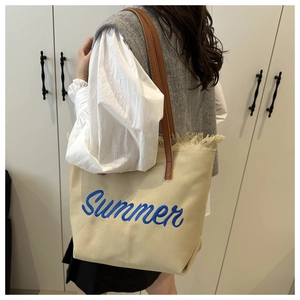 Detail of beige canvas tote bag with blue Summer embroidery and brown leather straps