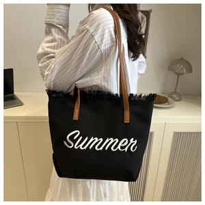 Detail of black canvas tote bag with Summer embroidery and brown leather handles