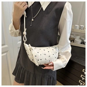 Close-up of white crescent bag with black bow embroidery and unique knotted shoulder strap