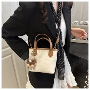 Detail of embossed cream crossbody bag with contrast brown handle and plush charm