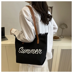 Detail of black canvas tote bag showing summer embroidery and tassel fringe decor