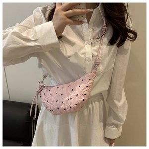 Detail view of pink dumpling bag with black bow embroidery and knotted strap worn by model