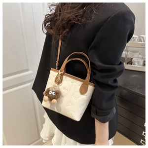 Detail of cream white bucket bag with embossed animal patterns and brown plush charm