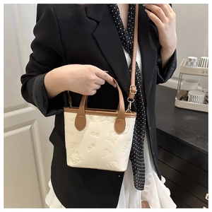 Detail of crossbody bucket bag with 3D embossed patterns and stylish brown handles