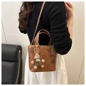 Detail of a brown leather bucket bag with embossed patterns and a cute plush doll charm