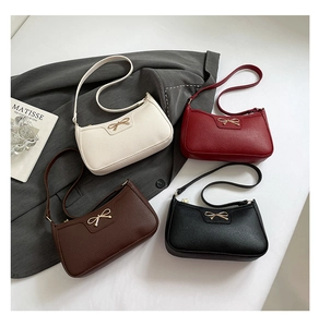 Flat lay of four textured leather shoulder bags with gold bow accents on a gray blazer