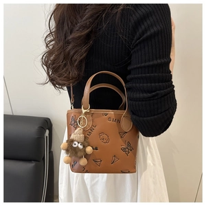 Detail of brown leather bucket bag featuring cute cartoon prints and a plush bear charm