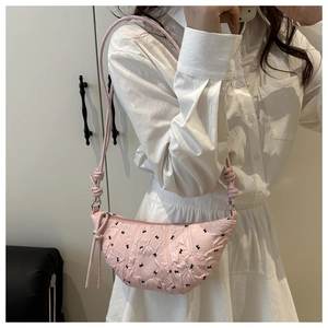 Close-up of pink quilted crescent bag with black bow patterns and knotted strap detail