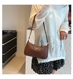 Close-up of a brown pebble leather baguette bag with a golden bow metal buckle detail