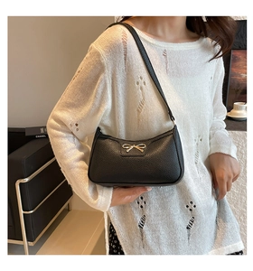 Detail of black pebbled leather underarm bag with gold bow clasp on female model